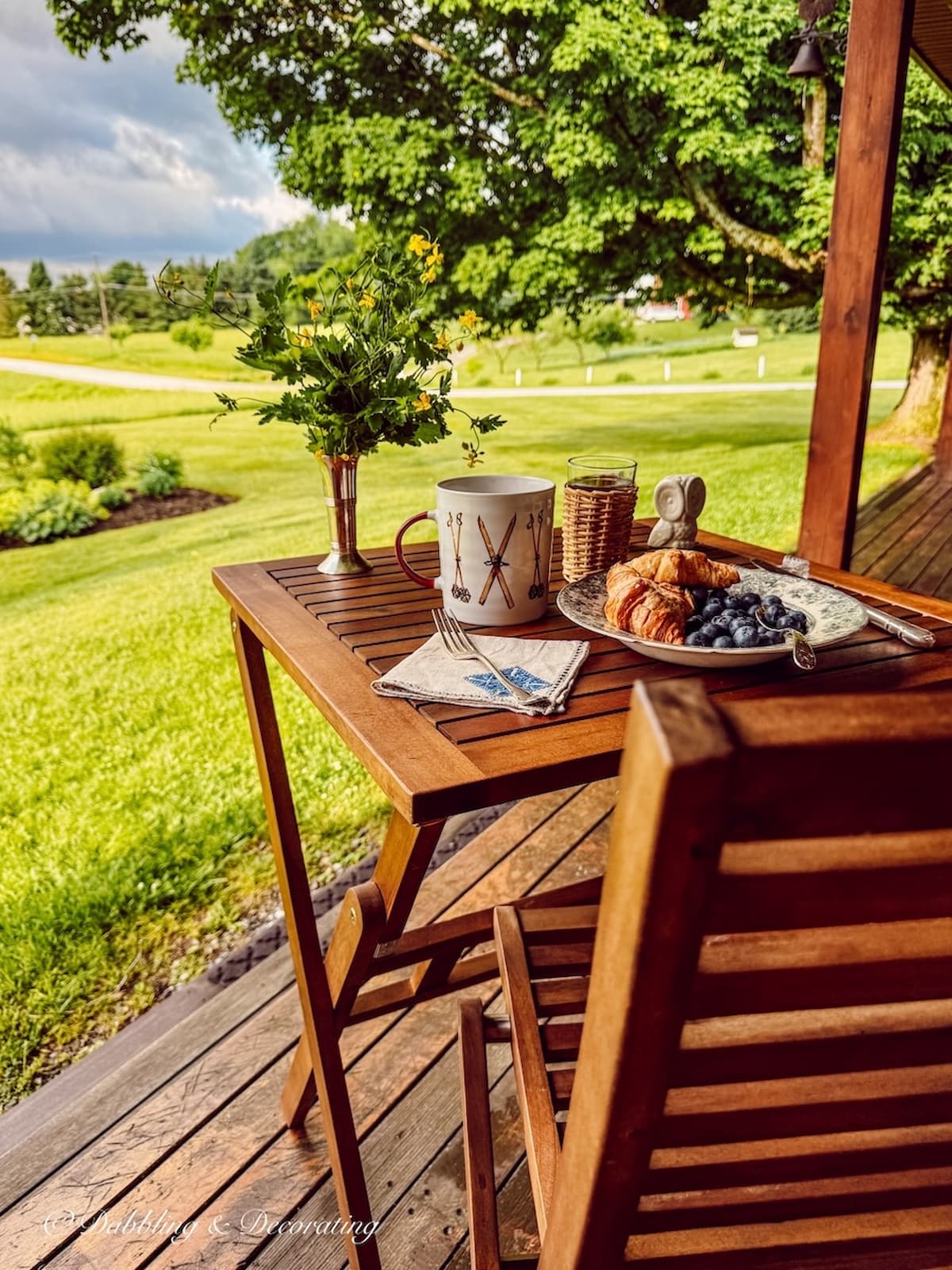 Table for one: a wooden teak table with chair set for breakfast on covered porch with stormy mountain views.