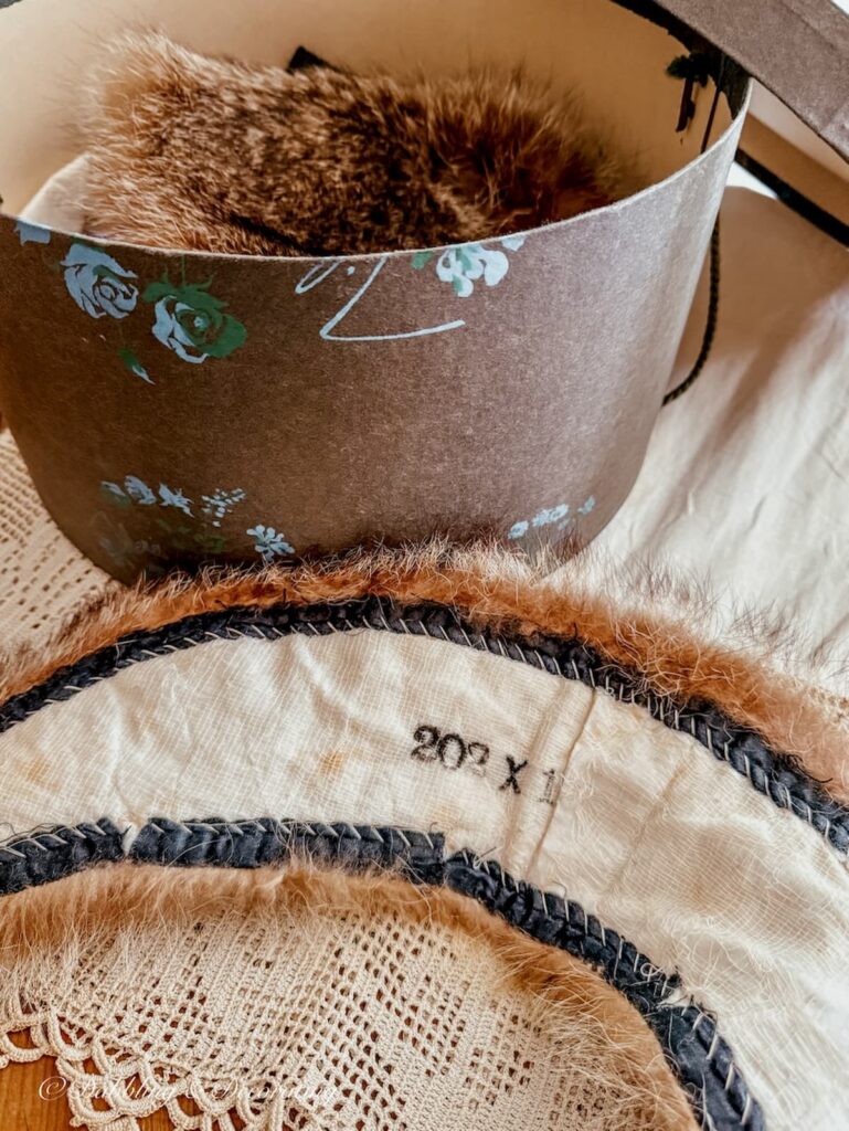 Antique raccoon collar upside down on table sharing it's size next to an old hat box.