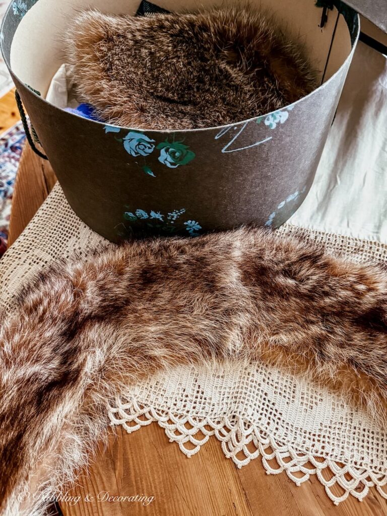 Antique raccoon collar laid out on table next to a hat box with an old fur hat.