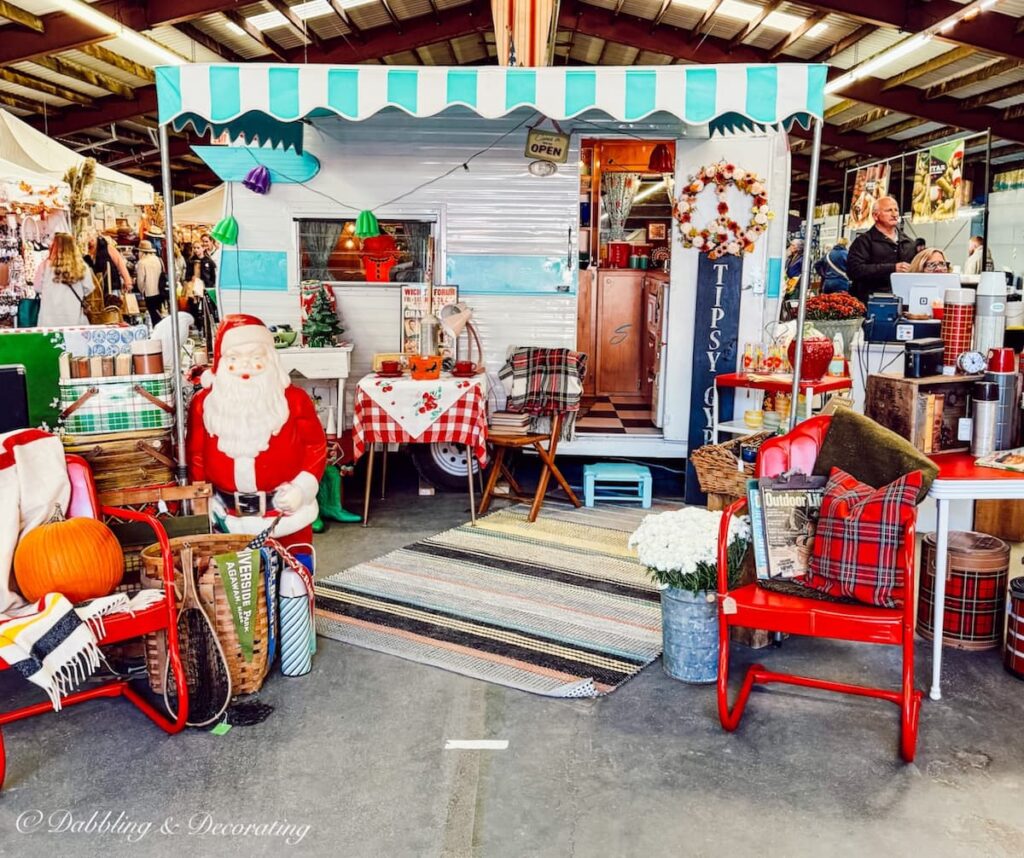 Tipsy Gypsy camper fall vintage booth display styled for fall and Christmas with colorful details like a Santa Clause with a pumpkin resting next to it.