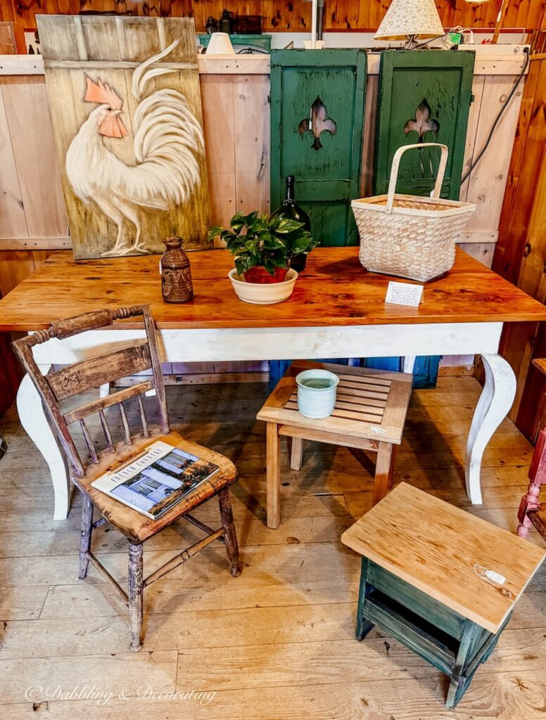 Minimalism fall vintage booth display ideas with a single French Country Book on old chair with fall scene to the rustic rooster painting and green shutters. The colors and styling are beautiful for fall.