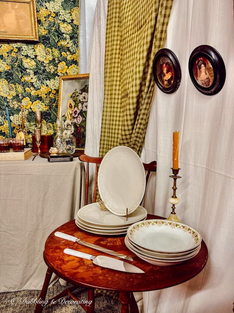 Antique booth display at Market Days with serving table and antique dishes displayed with curtain and two framed paintings on wall. Beautifully styled for fall.