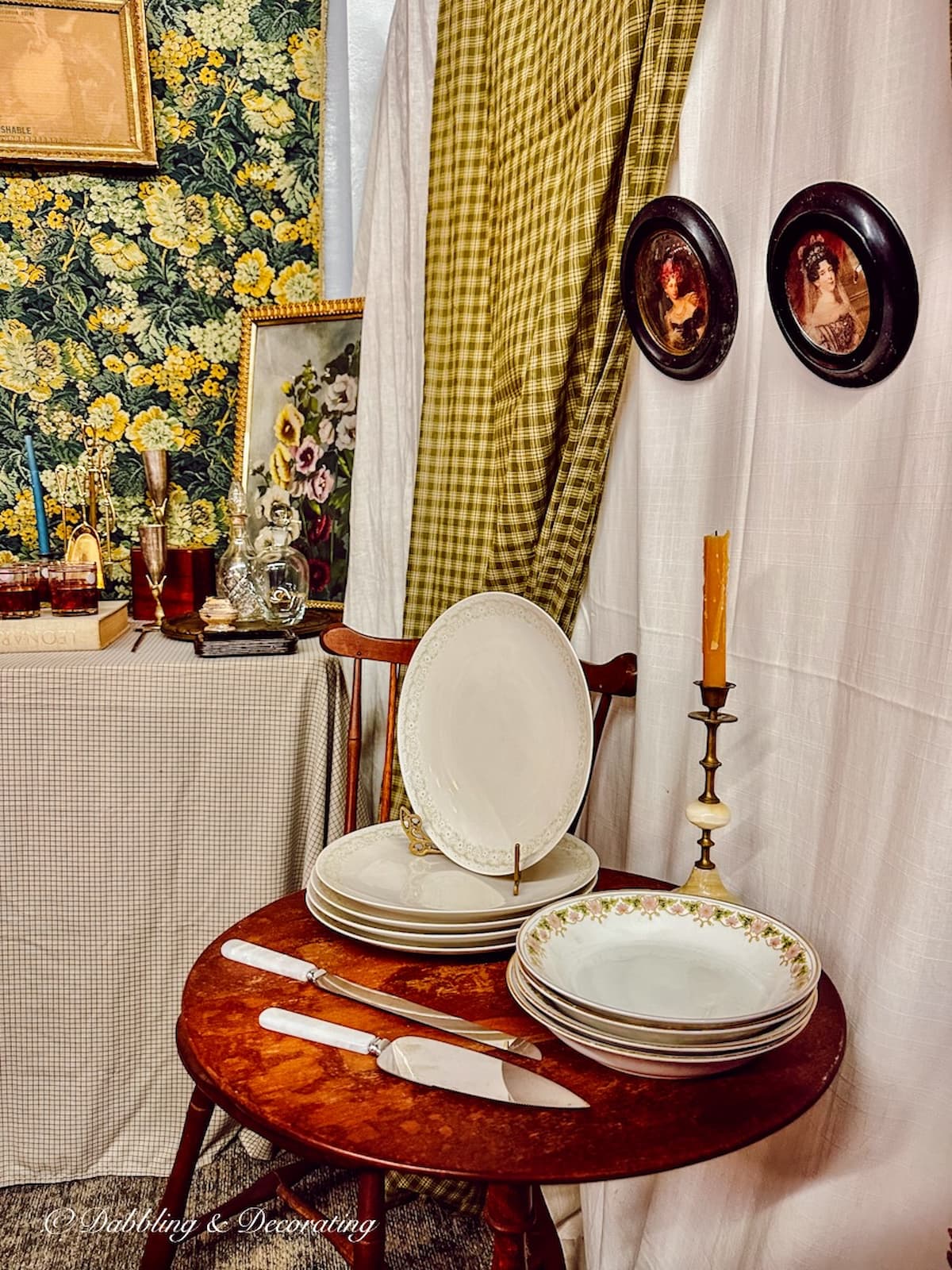 Antique booth display at Market Days with serving table and antique dishes displayed with curtain and two framed paintings on wall. Beautifully styled for fall.
