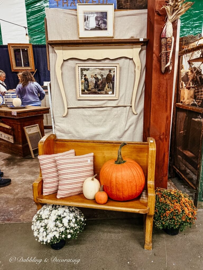 Vintage fall booth display with simplicity and a small mantel hanging on the wall with a church pew styled with pumpkin, pillows and mums at Vintage Market Days.