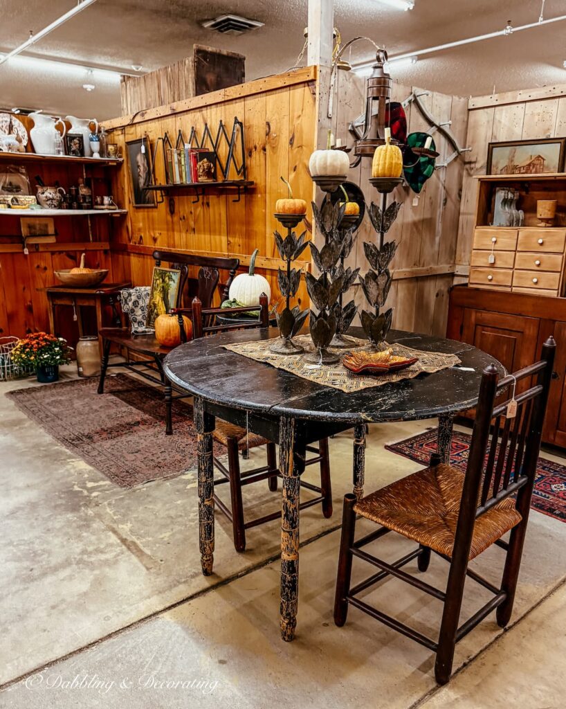 Fall vintage booth with round black table and chairs with tall candlesticks topped off with orange and white pumpkins at Stone House Antiques in Vermont.