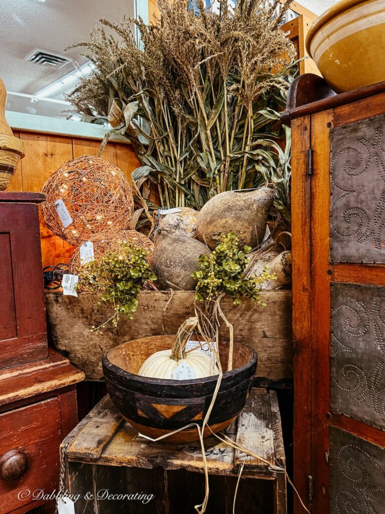Vintage booth displayed for fall with natural elements: corn brooms, pumpkins, gourds, and lit balls of twine all for sale.