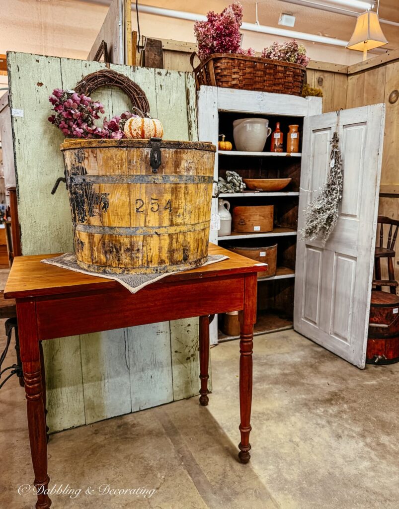 Vintage fall booth display with old hutch filled with Autumn finds and a table with a large crate and grapevine wreaths.