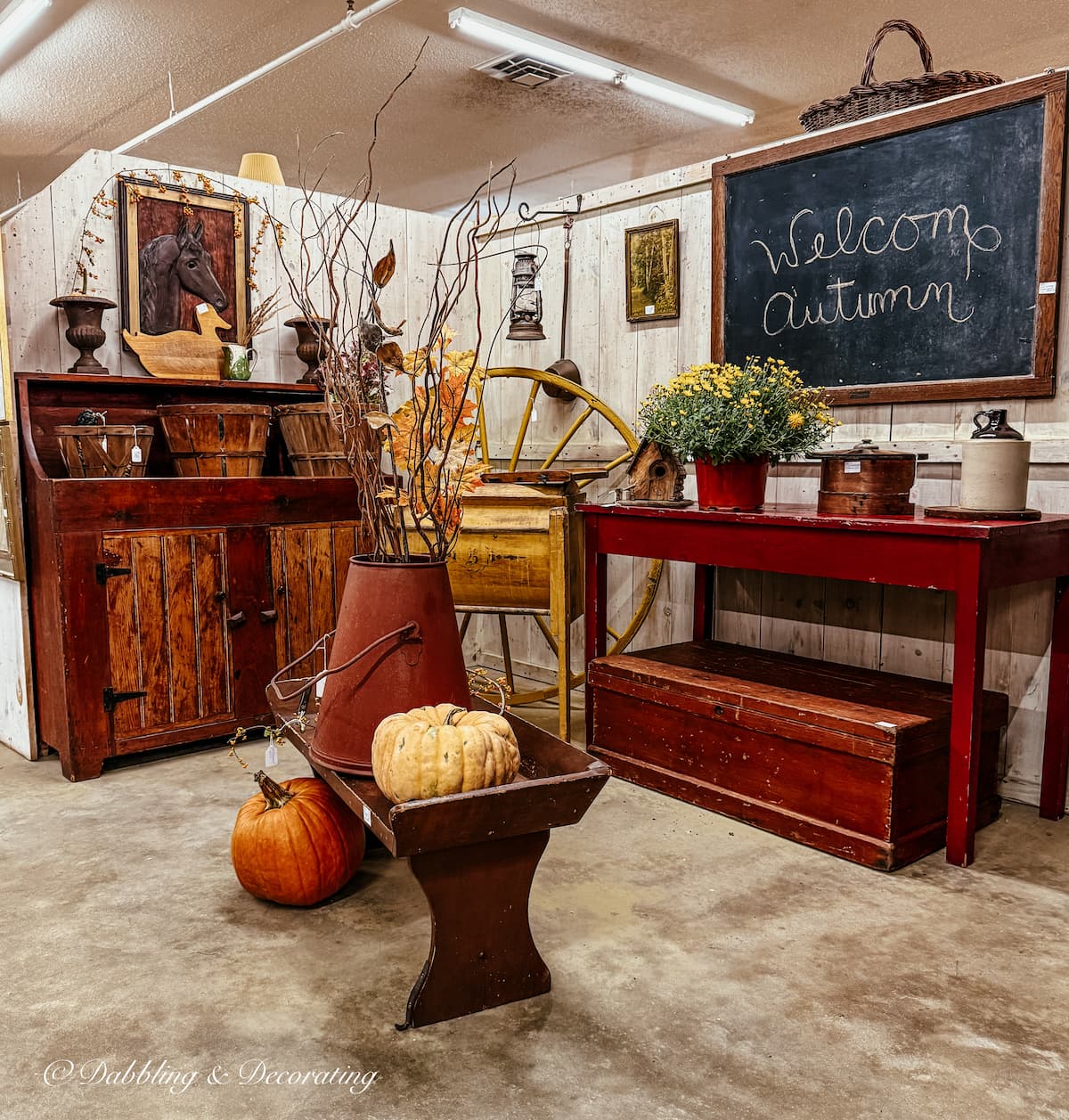 Fall vintage booth styled with deep reds, old branches and mums. Large red primitive table, chalkboard hanging that says Welcome Autumn. So inviting and warm.