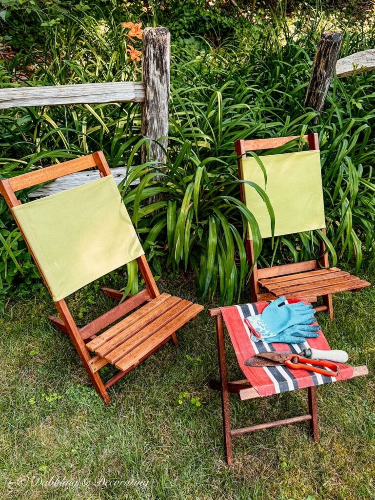 Two thrifted retro camp chairs with green canvas and wooden with camp stool and vintage garden tools in summer backyard garden display.