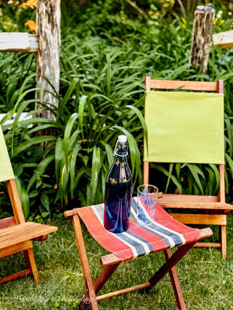 Retro camping chairs with green canvas and small camp stool with red canvas positioned in summer garden.