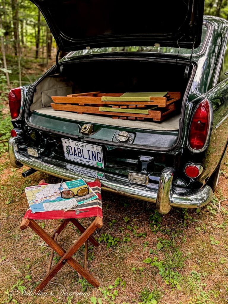 Vintage Volkswagen Fastback with retro camper chairs inside open trunk and camp stool with vintage road map and car keys in the woods on a Sunday drive.