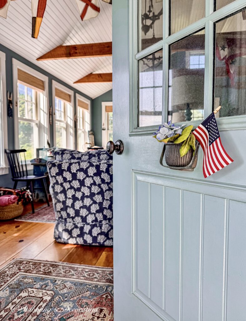 Open blue door with USA flag in Nantucket Basket Door knocker into a coastal inspired guest cottage with antique charm in Maine.