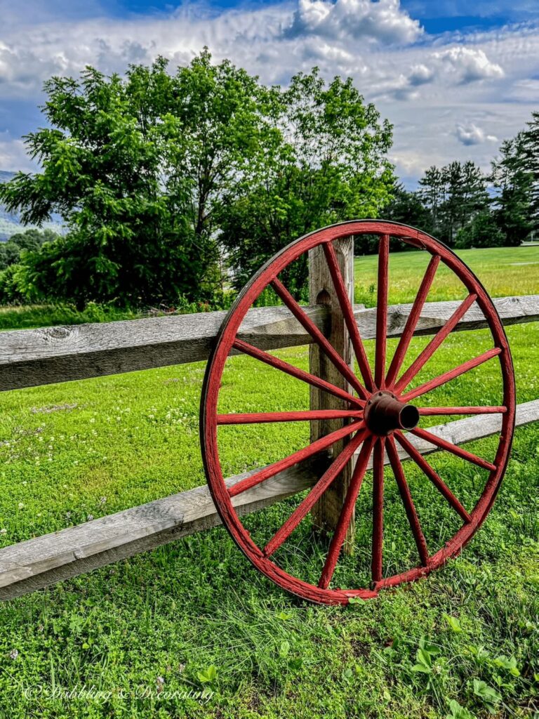 Painted red old wagon wheel leaning against a weathered split rail fence during the summer in the mountains.