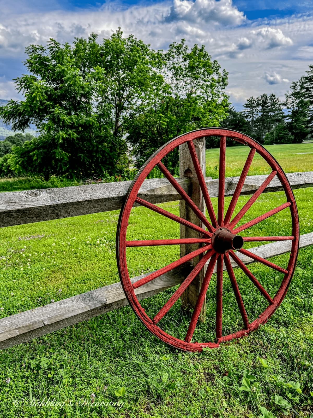 Painted red old wagon wheel leaning against a weathered split rail fence during the summer in the mountains.