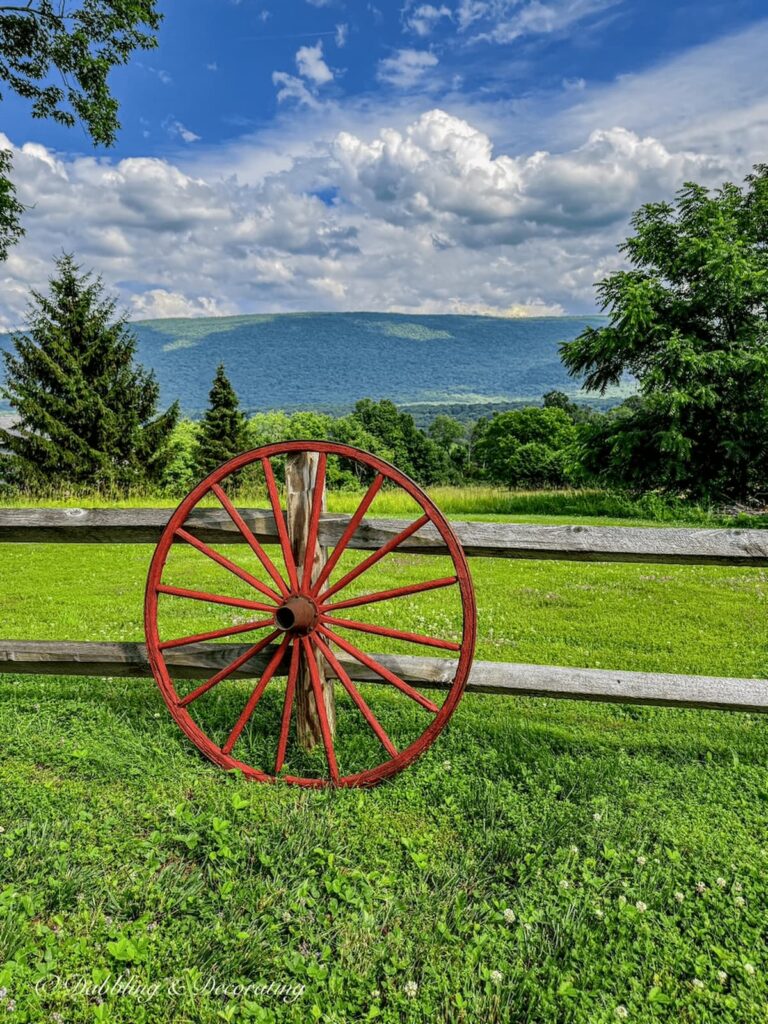 Old red wagon wheel decor with split rail fence with mountain landscape in summer.