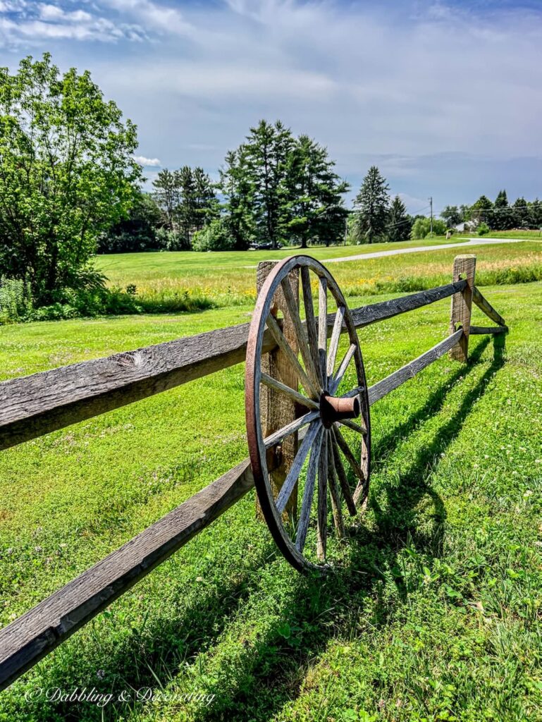 Weathered old wagon wheel leaning up against a weathered split rail fence during summer in the mountains.
