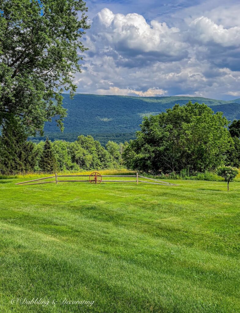 Old red wagon wheel against a split rail fence with mountain landscape in Vermont.