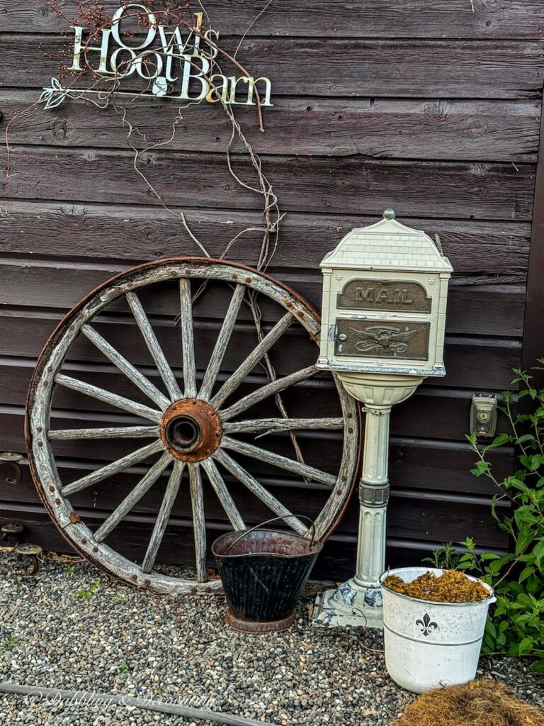 Weathered old wagon wheel leaning up against a barn with the sign Owl Hoot Barn at an outdoor wedding venue.