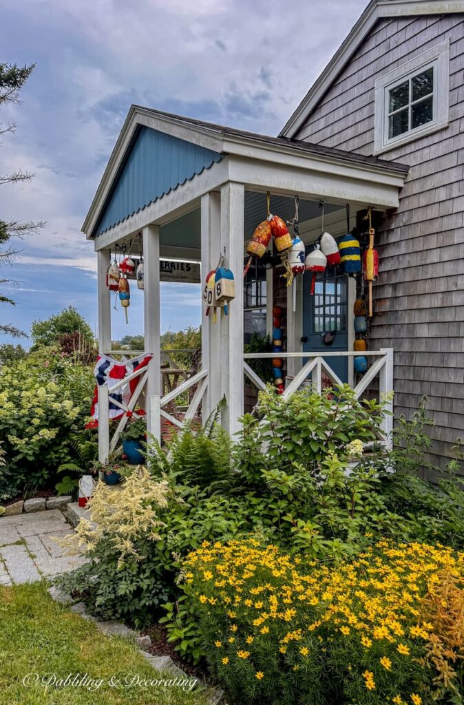 Seaside guest cottage in Maine with colorful New England details like cedar shakes, colorful lobster buoys, summer flowers, and patriotic bunting.