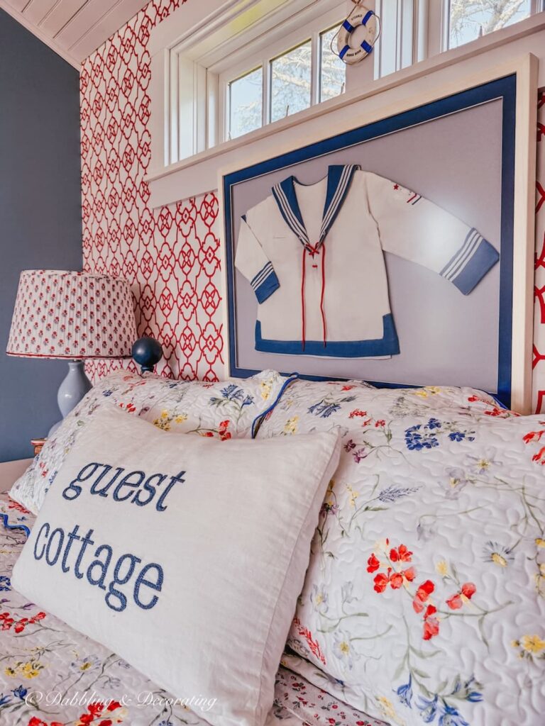 Framed children's sailor jacket on wall over bed in Maine guest cottage.