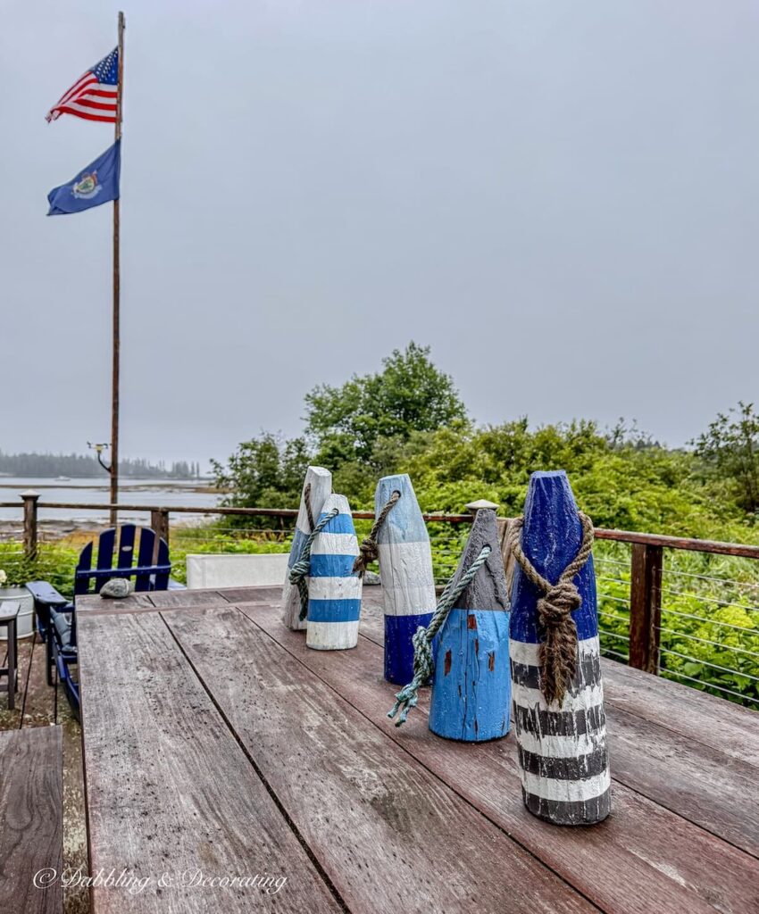 Weathered table and benches with blue and white lobster buoys lined up on an outdoor table on an overcast summer evening in Maine.