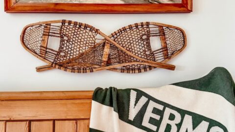 Vintage ski lodge corner styled with a Vermont blanket, vintage church pew, snowshoes on wall and winter painting.