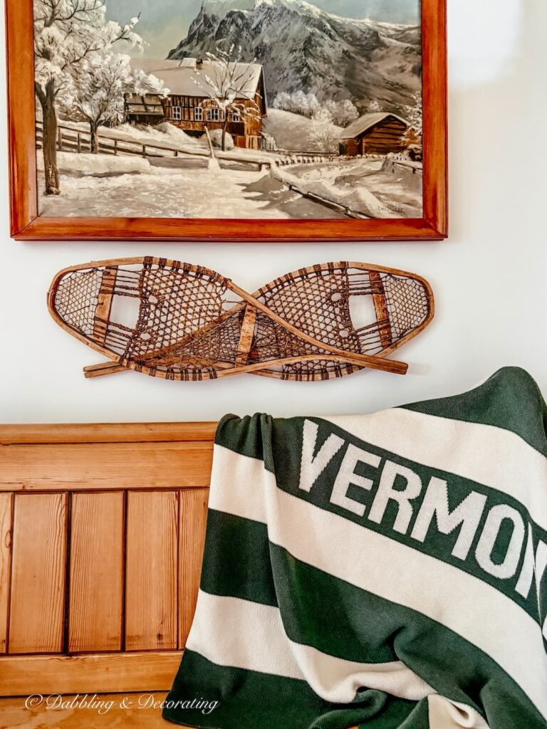 Vintage ski lodge corner styled with a Vermont blanket, vintage church pew, snowshoes on wall and winter painting.