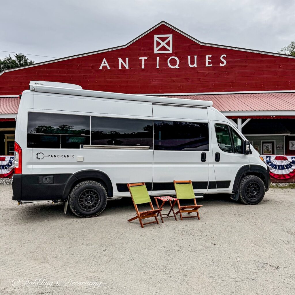 Panoramic White RV Van in front of red Hay Fields Antique Store in the Adirondacks with two vintage camping chairs
