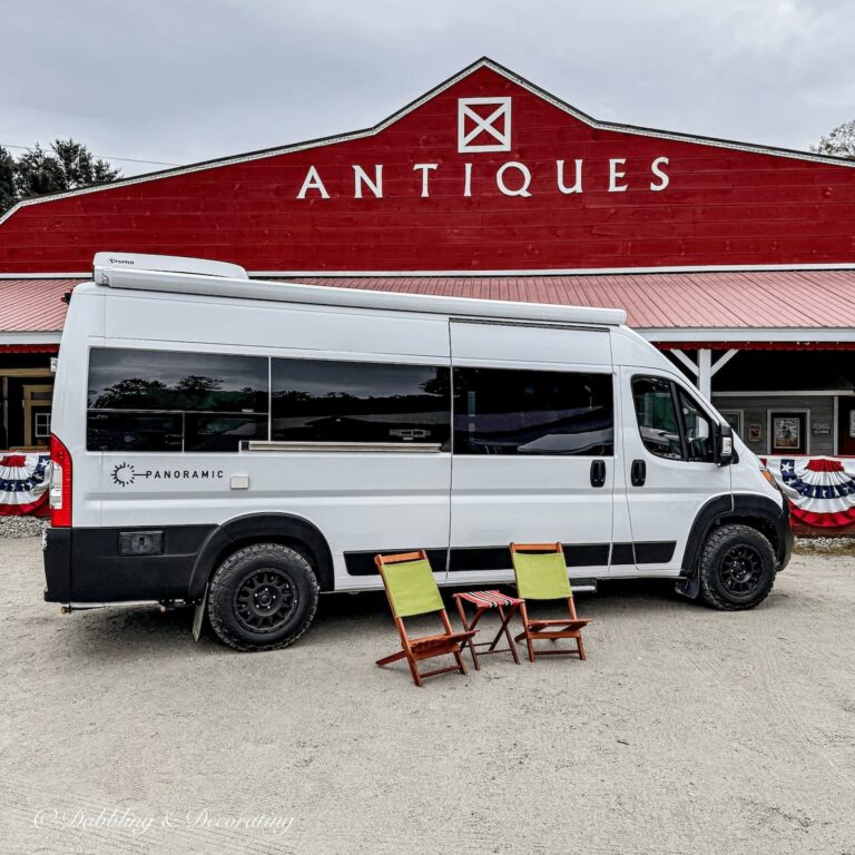 Panoramic White RV Van in front of red Hay Fields Antique Store in the Adirondacks with two vintage camping chairs