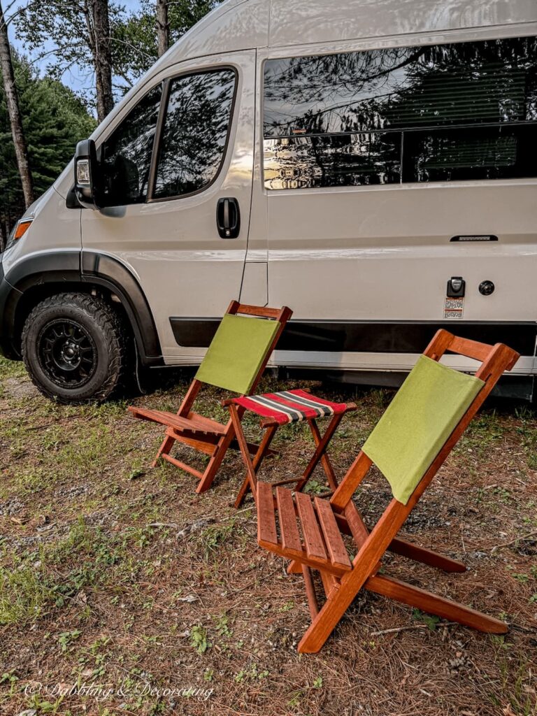 White RV boondocking in the evening with two teak camp chairs with green backings in the Adirondacks.