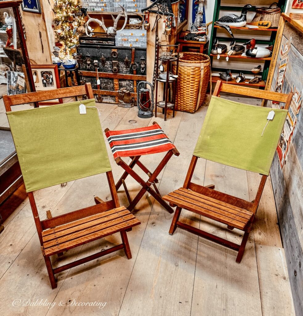 Two teak vintage camping chairs with green fabric and a small red and black camping stool in antique store.