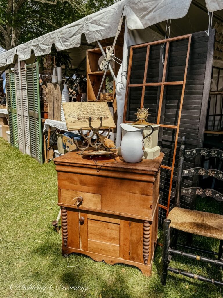 Antique wooden dresser display with coastal vintage finds up against of a wall of vintage shutters outdoors at Vintage Market.