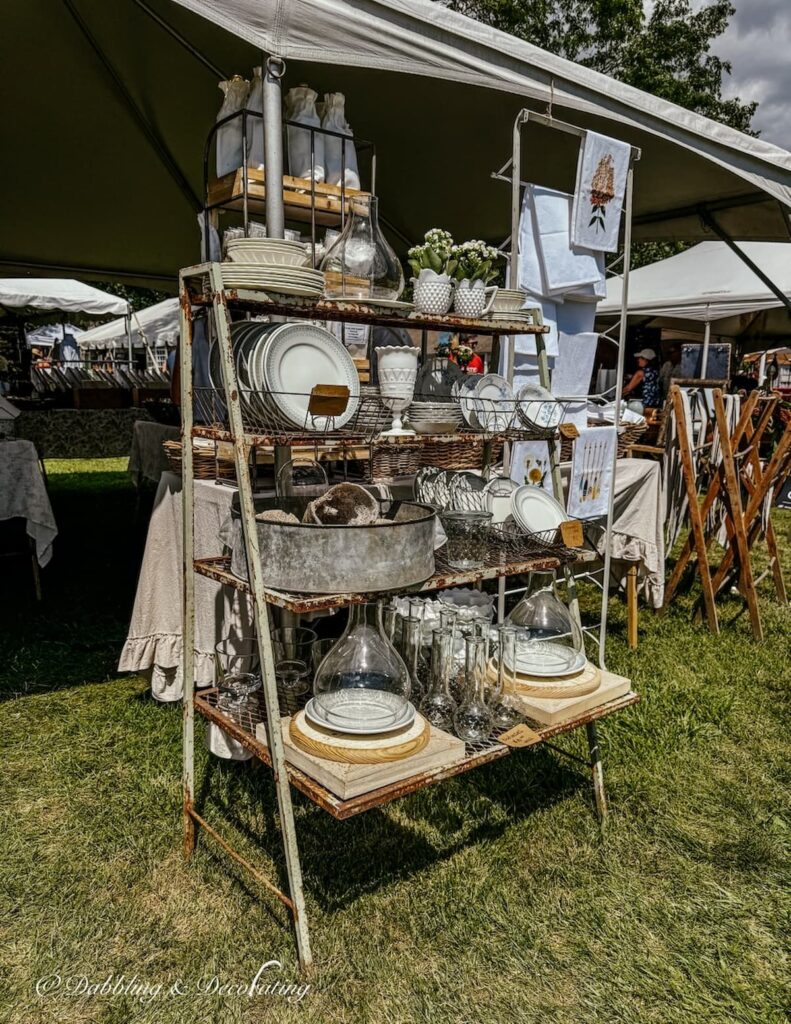 Vintage market display outdoors with vintage metal rack styled with vintage dishes and glassware.
