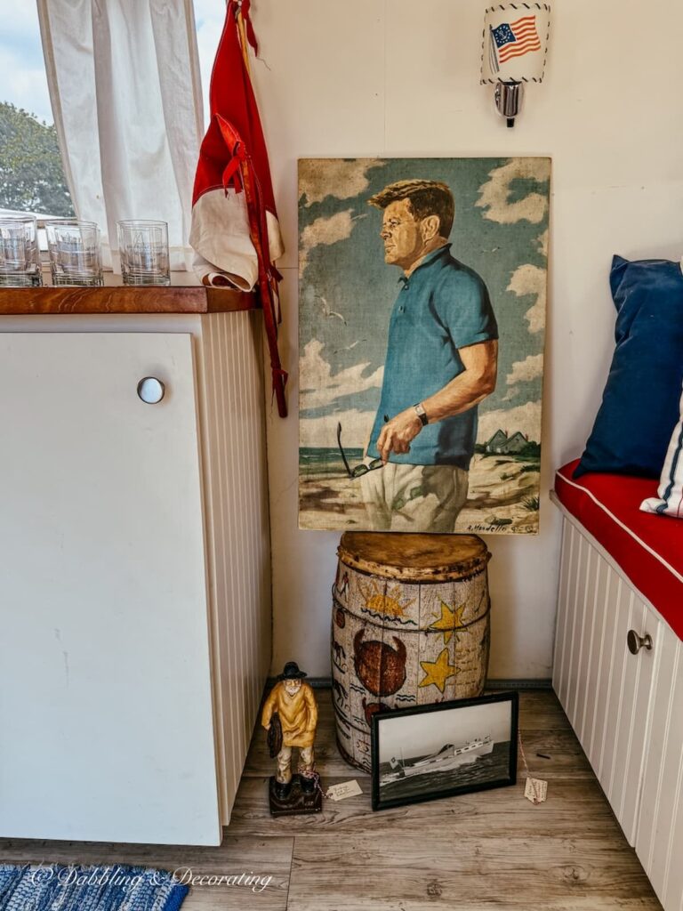 Antique booth display inside a air stream trailer with a John F. Kennedy painting, vintage maritime flags, and old barrel at Vintage Bazaar New England.