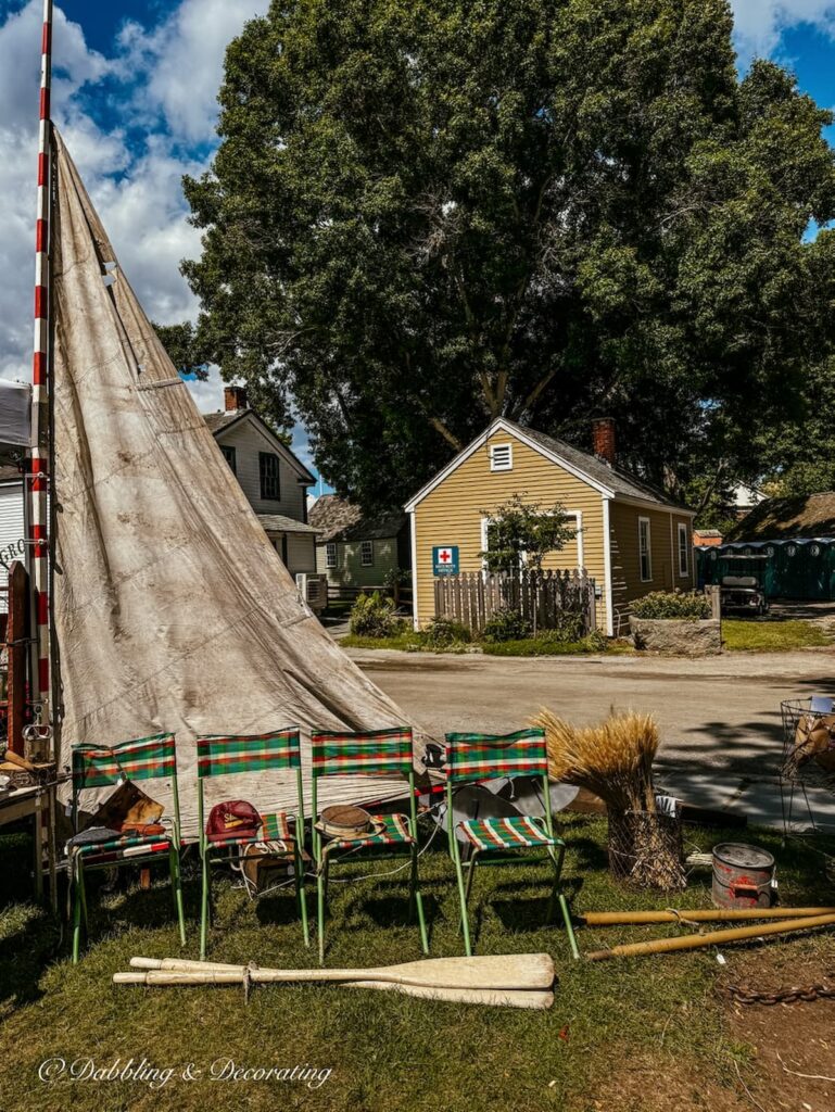 Old sailboat sail displayed at outdoor market booth display with vintage green camping chairs and old oars at Vintage Bazaar New England.