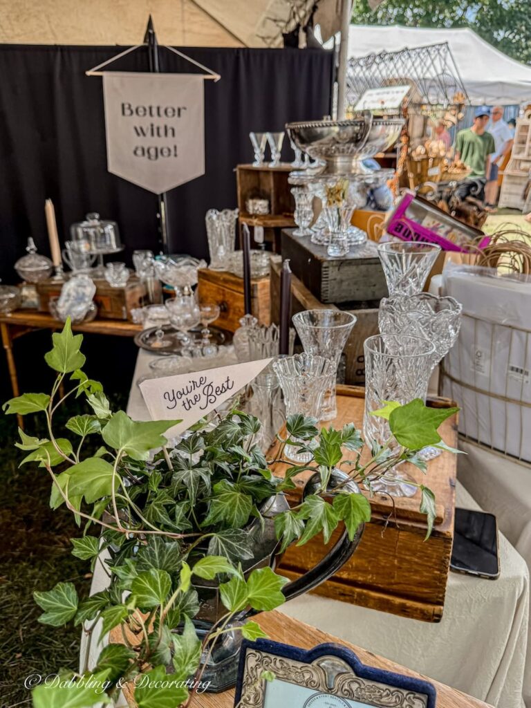 Vintage booth displayed with layered and stacked crystal and glassware with a sign that says Better with Age.