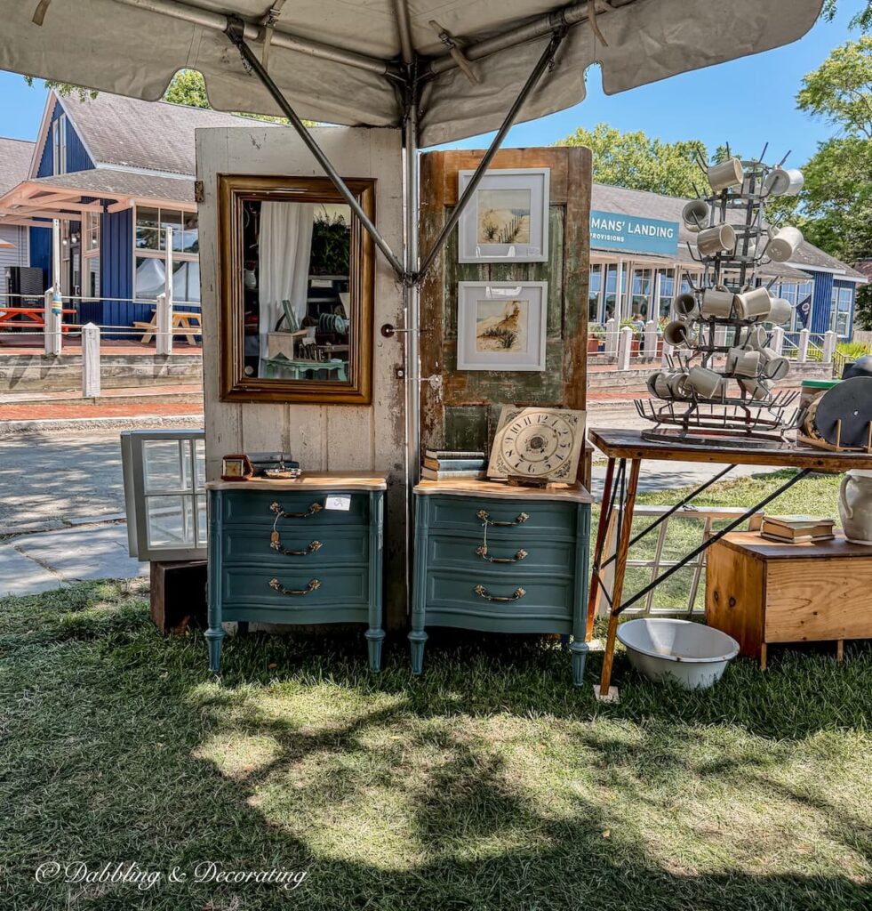 Antique booth corner display outdoors with old doors as backdrops for paintings and two blue dressers.