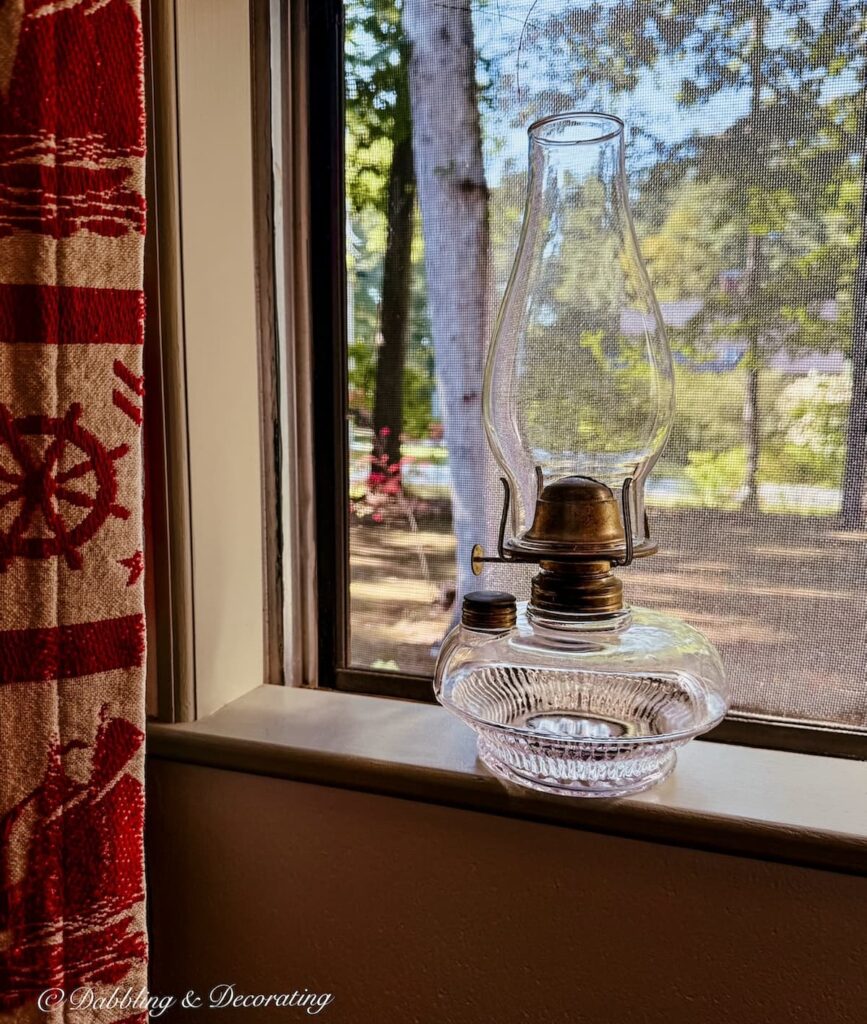 Antique oil lamp on windowsill next to coastal curtain on a rainy summer day.