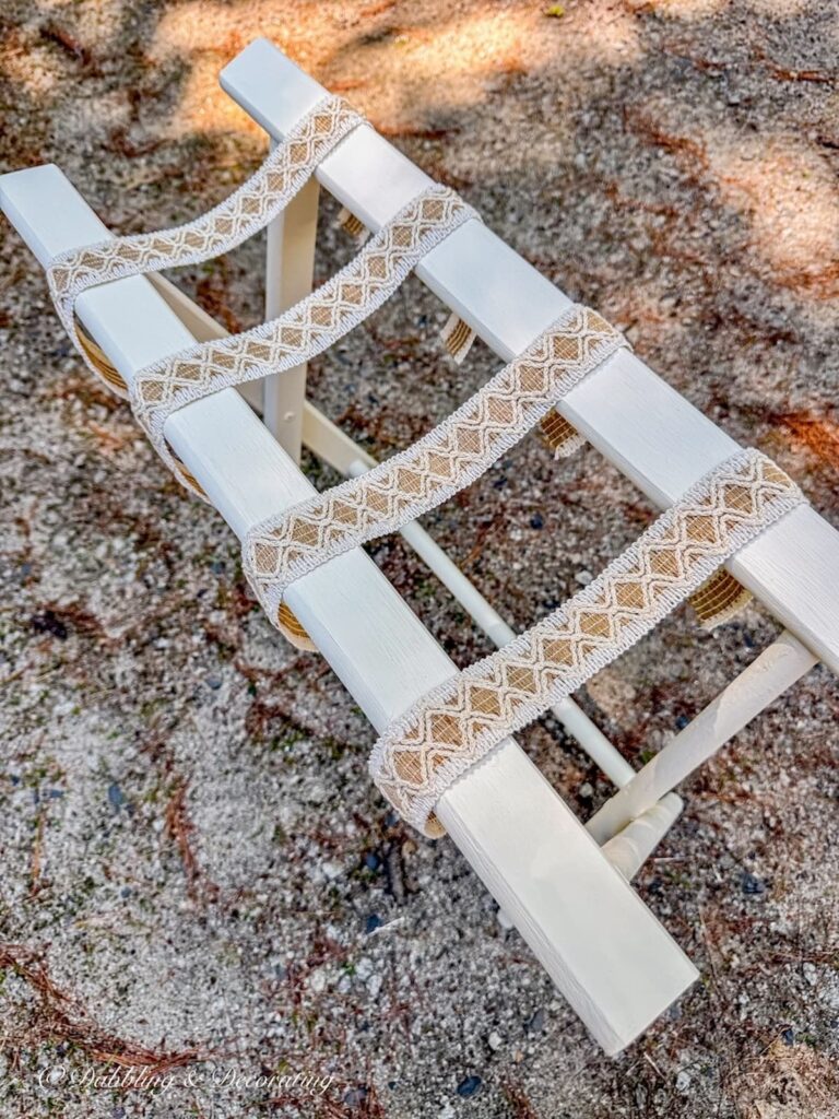 Painted folding luggage rack makeover with draped ribbon before securing it to the suitcase rack.