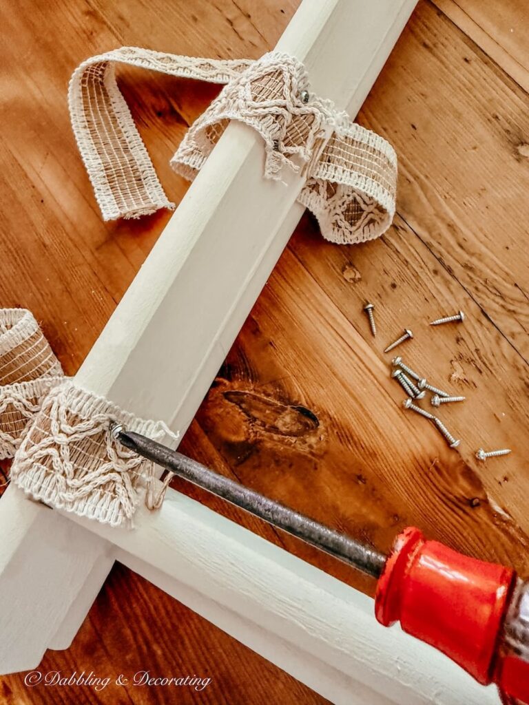 DIY luggage rack painted white with neutral jute ribbon being screwed in up close for tutorial