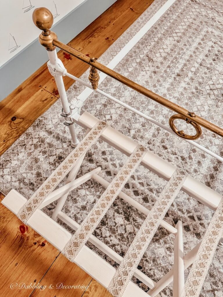 Folding suitcase rack painted white with ribbon details at the foot of an antique white wrought iron bed with brass details in bedroom makeover.