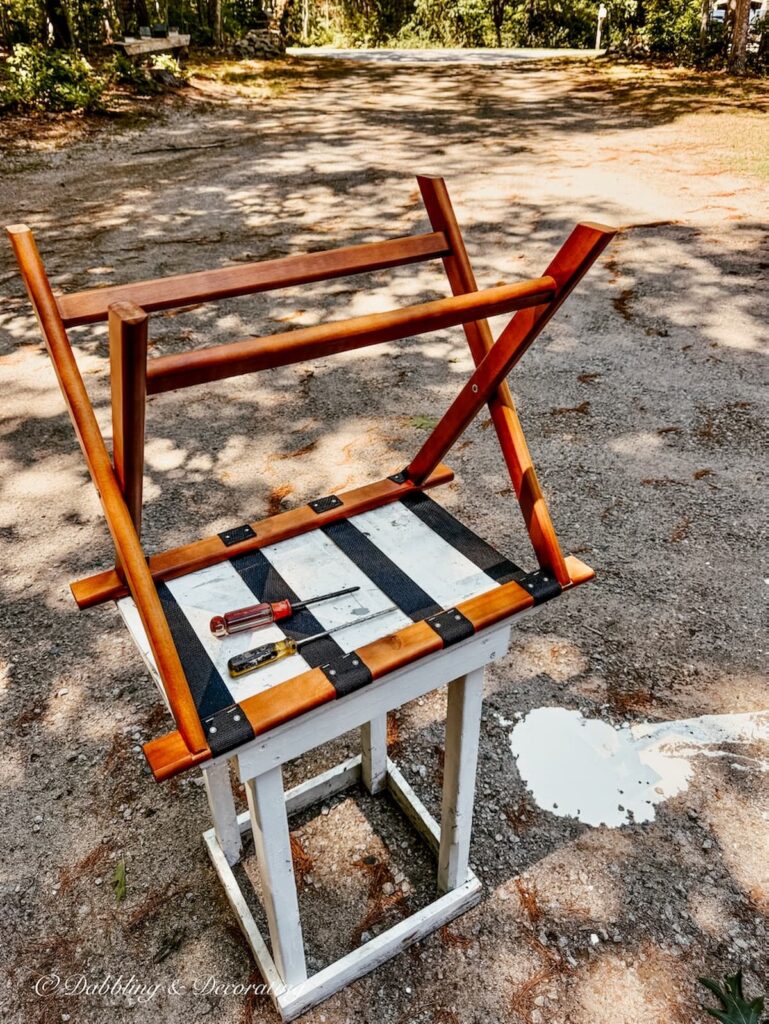 DIY folding luggage rack before painting upside down outside on table with spilt chalk paint on driveway.