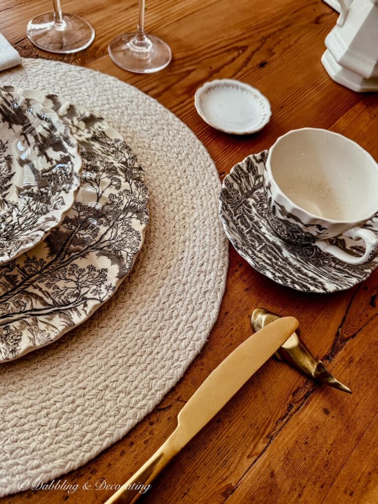 Brown and white transferware place setting close up with knife resting on a table's brass whale knife rest.