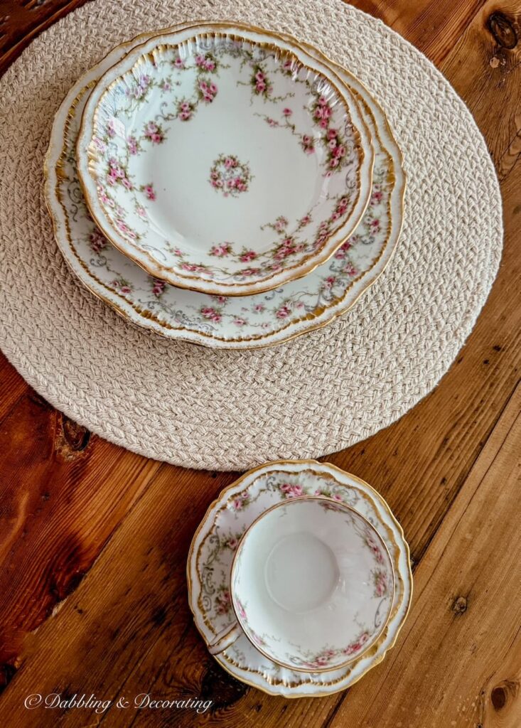 Pink and gold Theadore Haviland Limoge family heirloom place setting on antique wooden table.