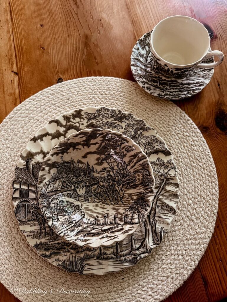 Brown and white transferware family heirlooms place setting on white tablecloth on antique wooden table.