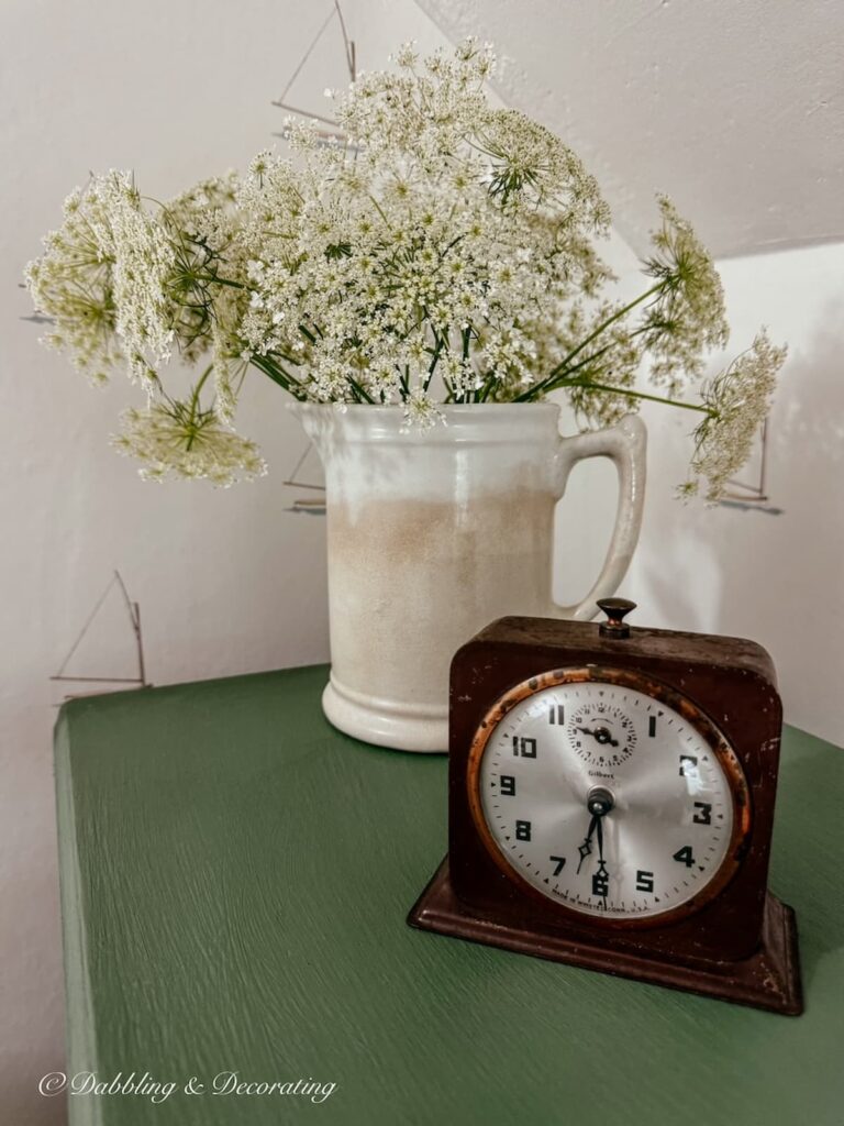 Ironstone pitcher with Queen Anne's Lace, an antique alarm clock on a painted nightstand makeover in green with sailboat wallpaper in guest bedroom.