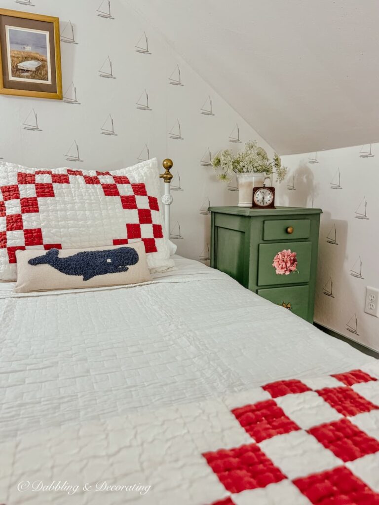 Painted nightstand makeover in green next to antique twin bed with red and white coastal style bedding, sailboat wallpaper in small attic bedroom corner.