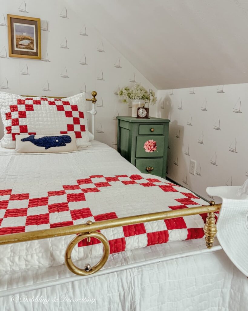 Attic bedroom with twin wrought iron antique bed with red and white bedding and a green painted nightstand makeover with sailboat wallpaper.