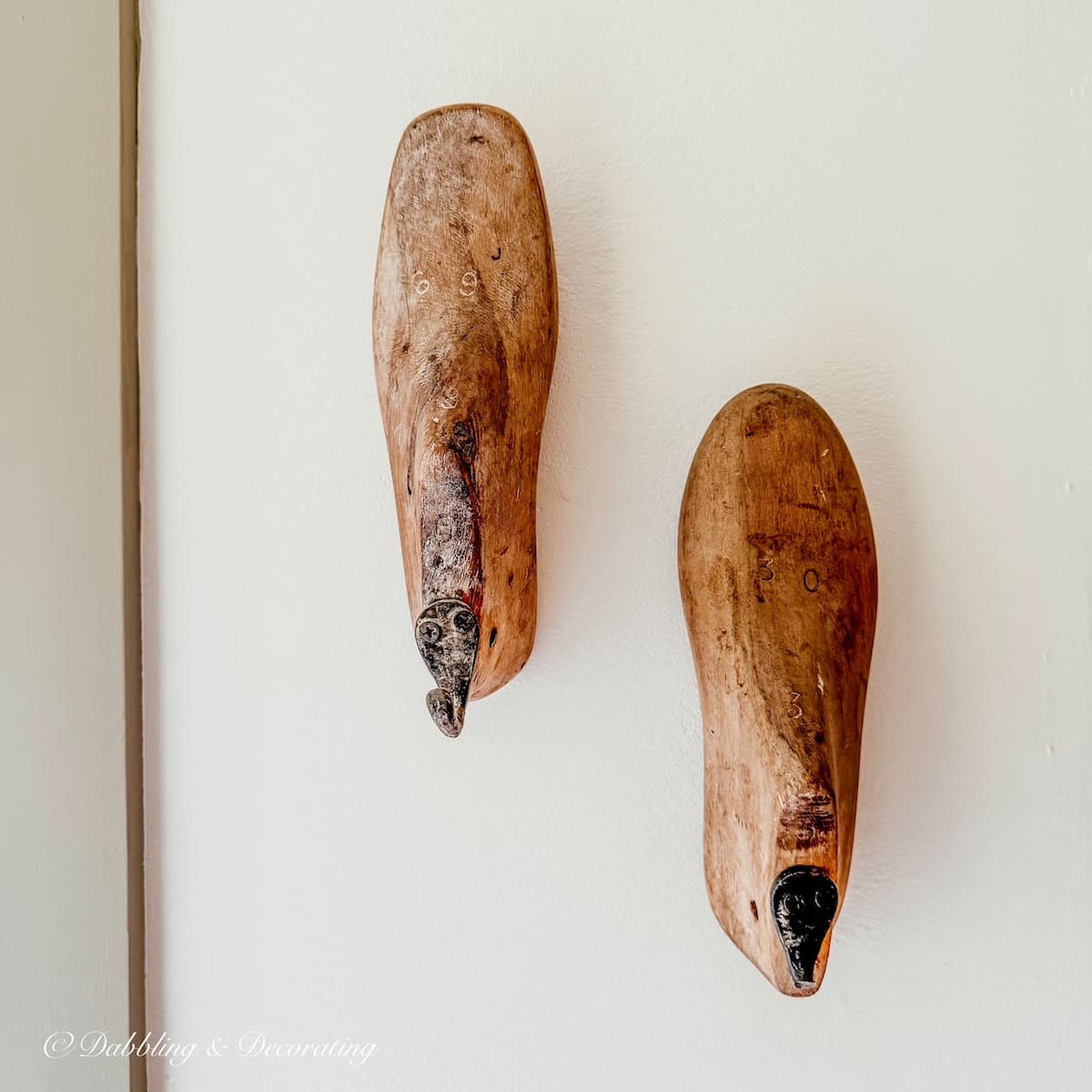 A pair of old wooden shoe molds hanging on a wall painted in Benjamin Moore's Simply white with Nantucket Gray trim.