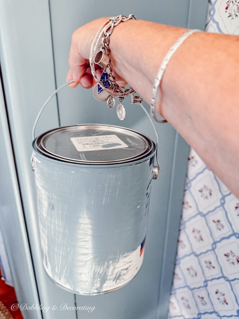 Can of custom blue-gray historic paint color in hand next to painted cabinet.